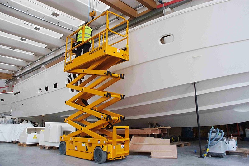 Podnośnik nożycowy Compact 2012DX podnosi pracownika do prac na wysokości przy burcie statku